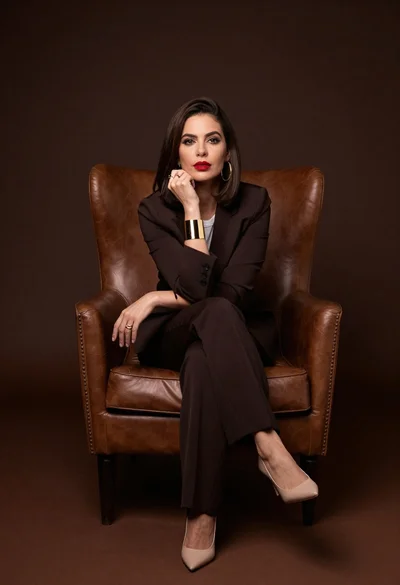 Poised woman in pantsuit seated on leather armchair
