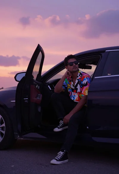 Man sitting on luxury car door against dramatic pink purple sunset sky