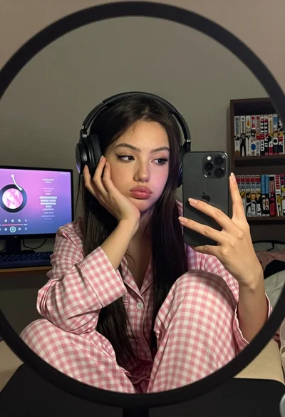 Young woman taking mirror selfie wearing pink checkered pajamas indoors
