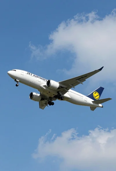 Commercial airliner flying across bright blue sky with scattered white clouds