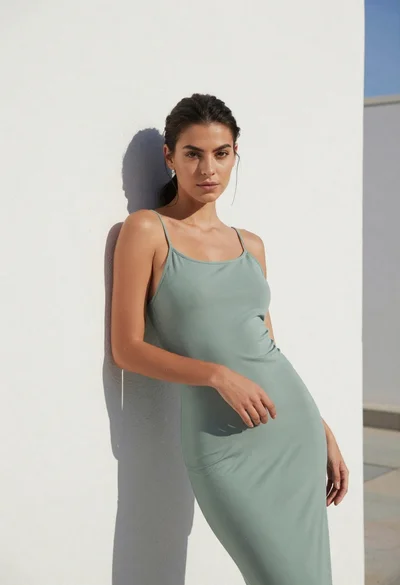 Young woman in sage green dress leaning against white textured wall