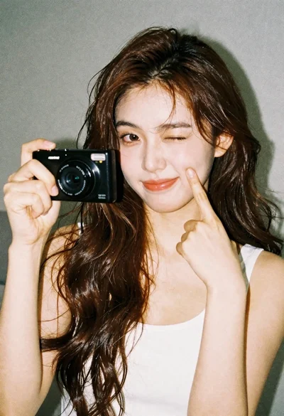 Young woman with brown hair holding camera and winking in indoor setting
