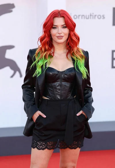 Young woman with red to green hair posing confidently on white backdrop