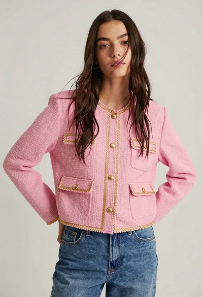 Young woman in pink jacket and blue jeans against light studio background