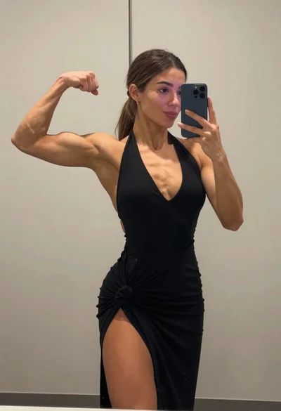 Muscular woman taking a mirror selfie flexing bicep in an indoor room