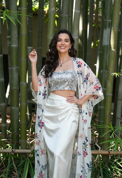 Smiling woman in silver top and white skirt within lush bamboo grove