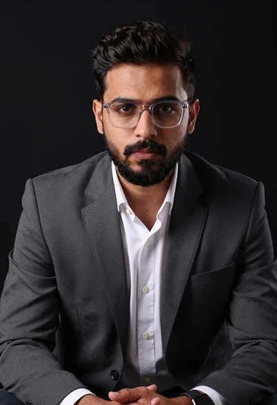 Professional portrait of man in dark suit jacket against solid black background