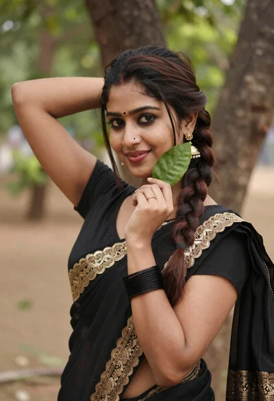 Young woman in black saree holding green leaf outdoors with soft smile