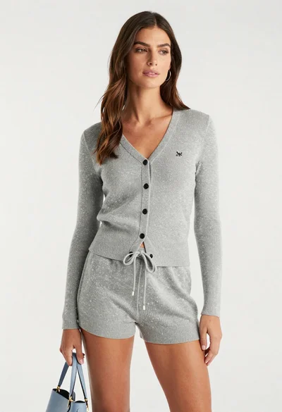 Woman with brown hair wearing grey cardigan and shorts studio portrait