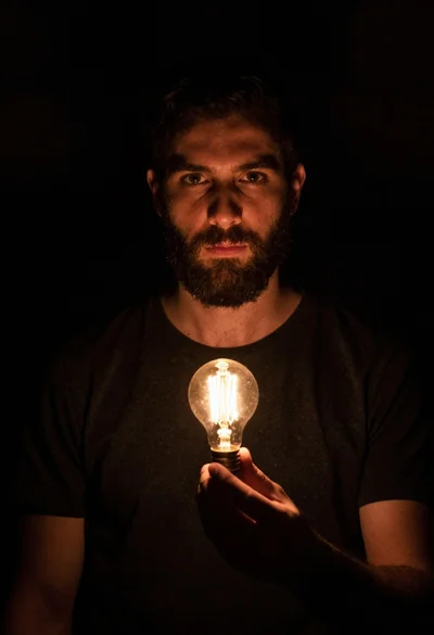 Bearded man holding illuminated lightbulb against black void