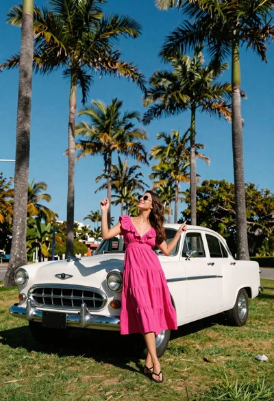 Woman in pink dress posing by vintage car under tall palm trees