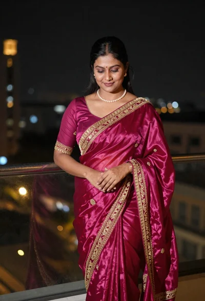Woman in magenta silk saree on balcony overlooking blurred city lights