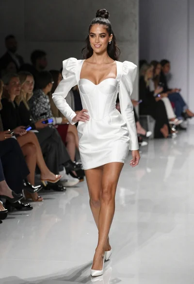 Confident woman in white satin mini dress walking on glossy runway