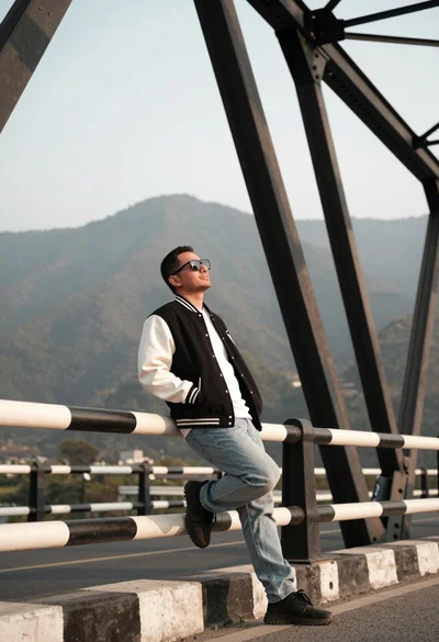 Man leaning on striped railing on bridge overlooking hazy mountains at golden