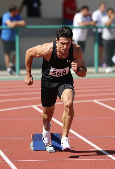 Muscular man sprinting on red track during bright daylight athletic competition