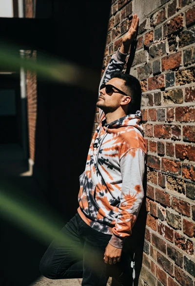 Man leaning against textured brick wall in an urban alleyway setting