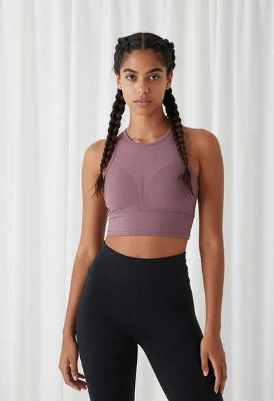Young woman in mauve crop top standing against sheer white curtains