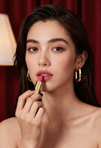 Close up portrait of woman applying pink lipstick against red curtains