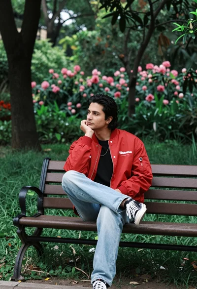 Man in red bomber jacket sitting thoughtfully on park bench surrounded by