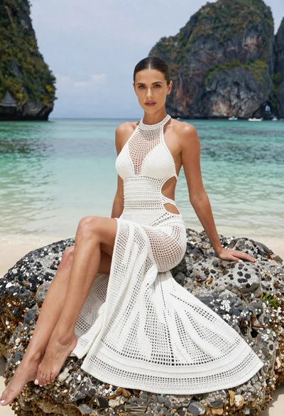 Woman in white crochet swimsuit sitting on rock by tropical sea