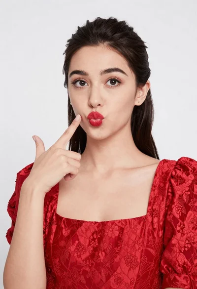 Young woman pointing playfully at cheek in deep red studio dress