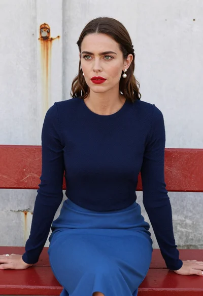 Woman with brown hair seated on red bench against weathered white wall