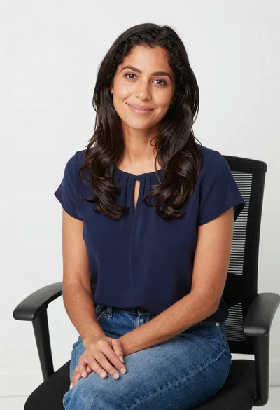 Smiling woman in navy top sitting on black chair against white wall