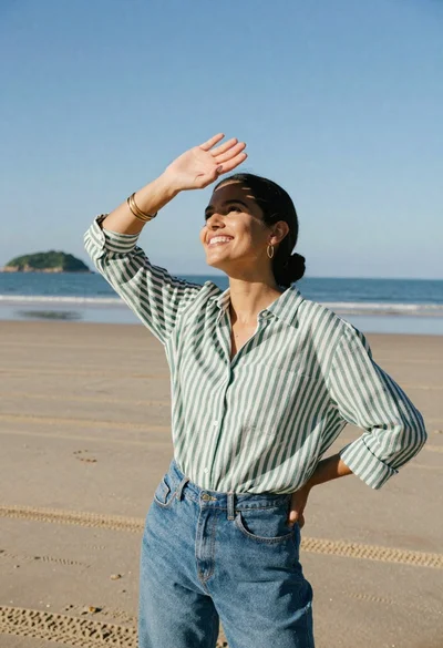 Joyful young woman shielding eyes on sandy beach under bright sun