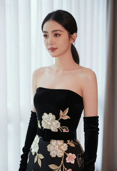 Poised woman in black embroidered velvet gown against soft white drapes