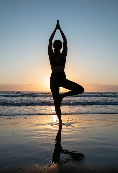 Silhouette of person performing tree pose on wet beach at sunset