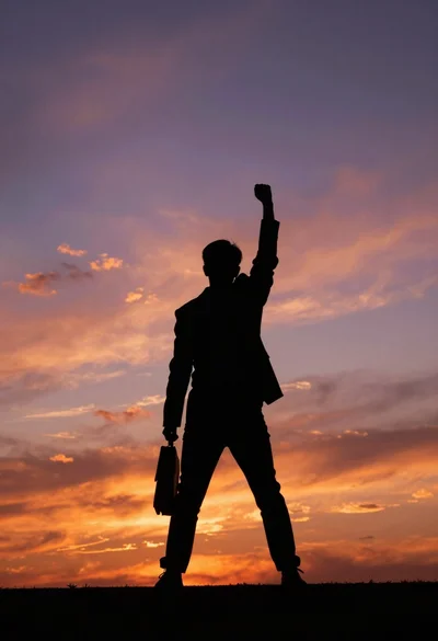 Silhouette of person standing triumphantly against vibrant sunset sky backdrop
