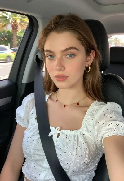 Fair skinned woman in white blouse seated inside car looking at camera