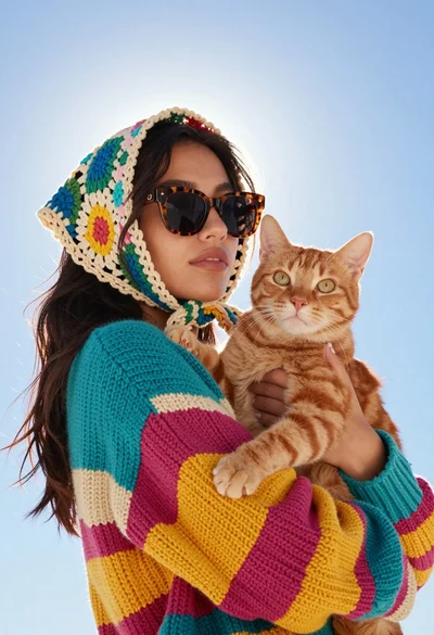 Young woman with cat wearing crocheted scarf under bright blue sky
