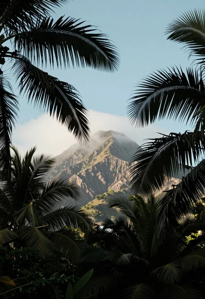 Serene tropical mountain landscape framed by lush palm fronds in soft daylight