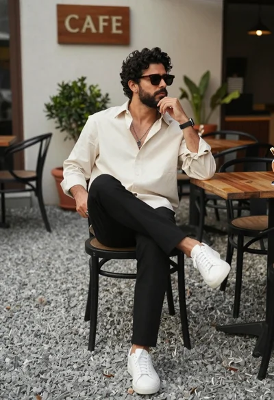 Stylish man with dark curly hair and beard sits in outdoor cafe