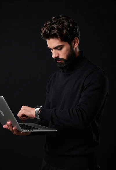 Man in black turtleneck checks watch with laptop under arm