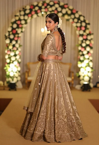 Woman in embroidered gold lehenga standing in floral archway interior