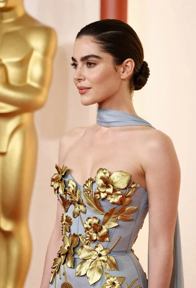 Woman in pale blue gown with gold appliqués against cream backdrop