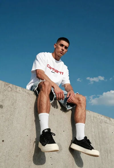 Young man sitting on concrete ledge under bright blue sky
