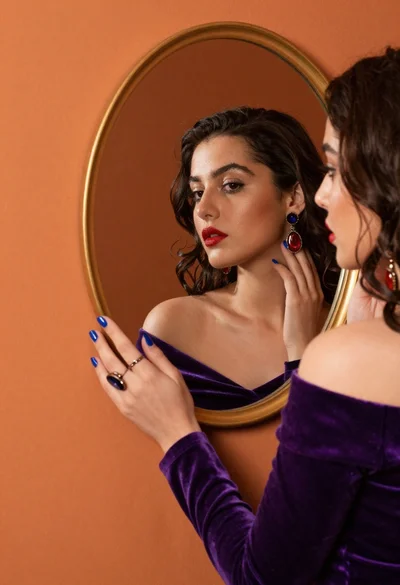 Woman in purple velvet looking into an oval mirror
