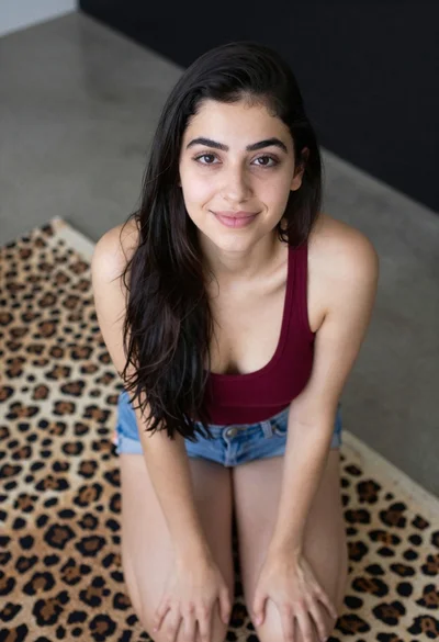 Young woman kneeling indoors wearing tank top and denim shorts