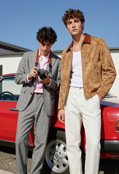 Two young men posing by vintage red car under bright blue sky