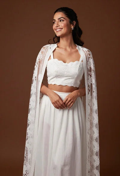 Smiling woman in white embroidered ensemble against textured brown studio backdrop