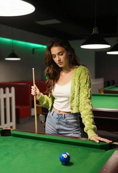 Young woman at pool table holding cue stick looking at eight ball