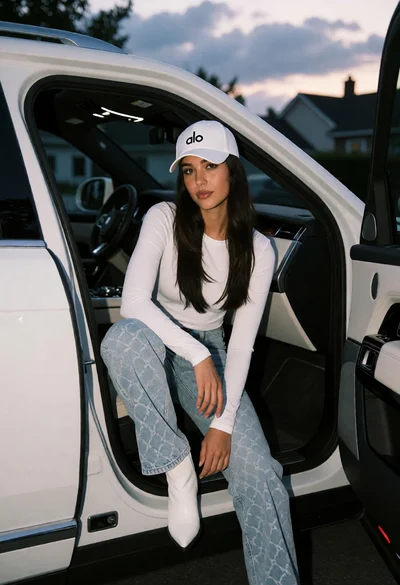 Young woman sitting on luxury suv door sill at dusk in residential