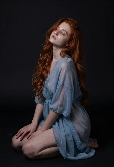 Woman with red hair kneeling in sheer blue dress