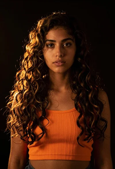 Young woman with dark curly hair lit by golden backlight