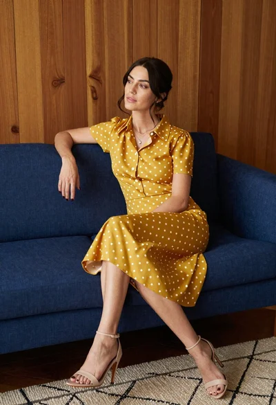Woman in mustard polka dot dress sitting on blue sofa indoors