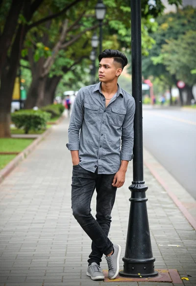 Young man leaning against black lamppost on paved park sidewalk outdoors