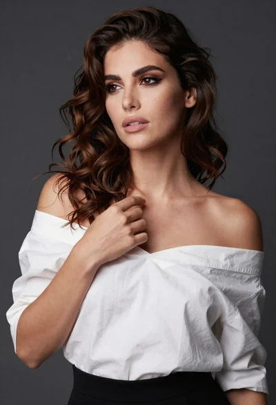 Poised woman in white top touching collarbone against dark studio background